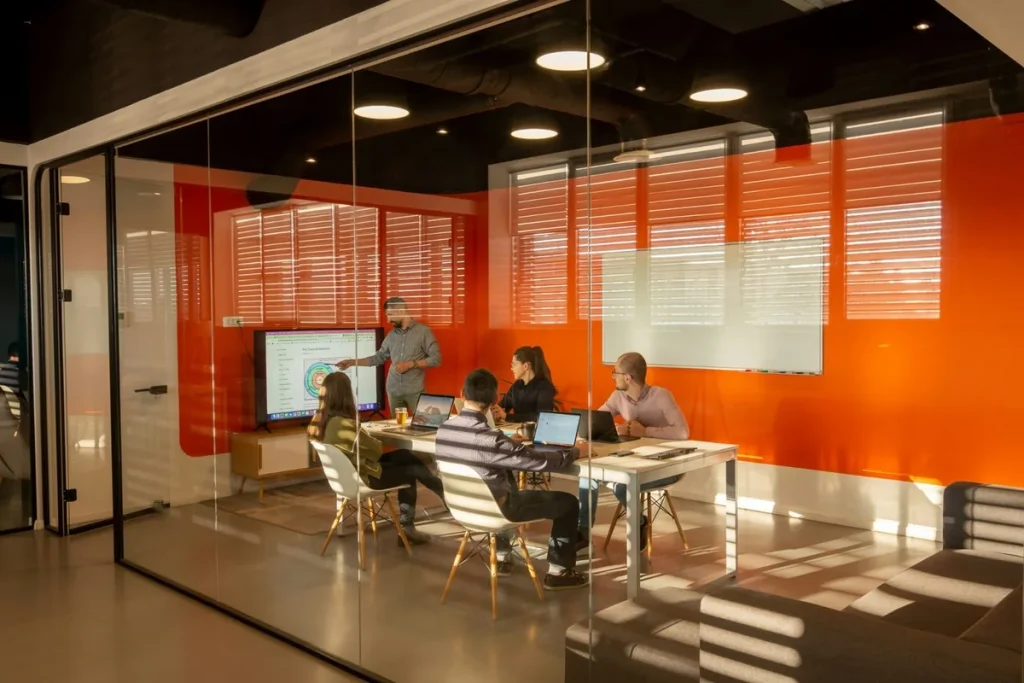 Beraterteam in einem verglasten Besprechungsraum mit orangefarbener Wand