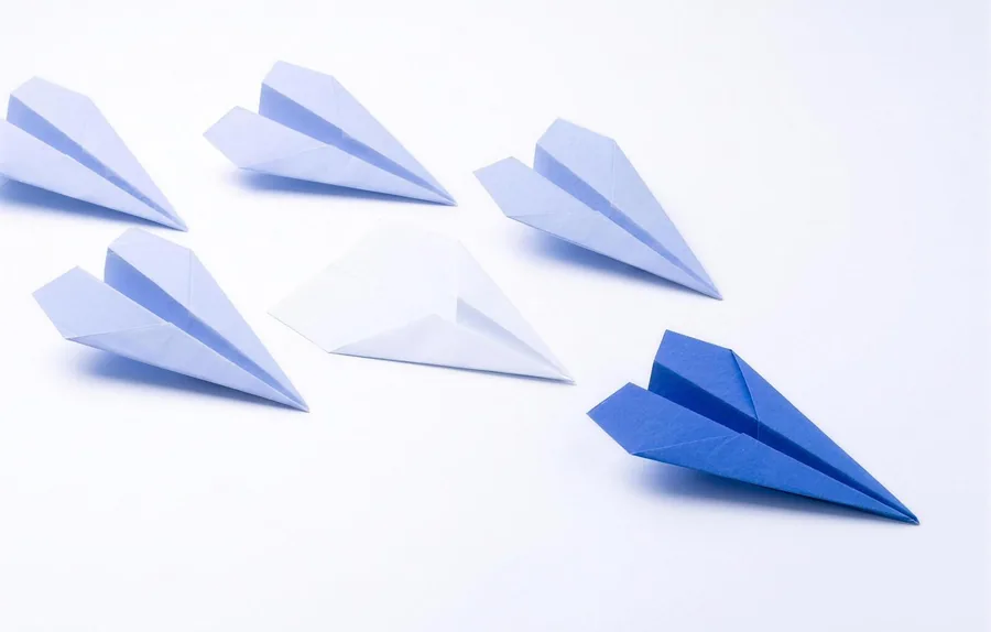 Ein blauer Papierflieger zwischen vielen hellen, leeren Fliegern